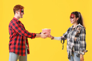 Young couple dressed for Halloween with popcorn on yellow background