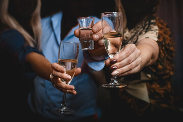 Hands of girls and men clinking glasses and a glass of alcohol close-up of the party