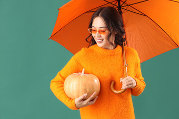 Young Asian woman in fall clothes with umbrella and pumpkin on green background
