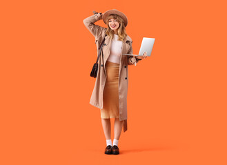 Stylish young woman in fall clothes with laptop on orange background