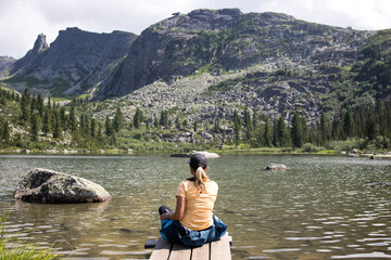 a girl tourist admires the views of the Ergaki mountains while sitting on the shore of Rainbow Lake