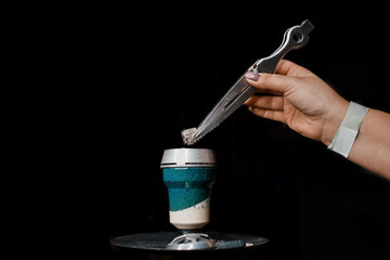 The hand of a girl with a special tool with tongs puts coal in a ceramic hookah bowl, an object to smoke in the dark background - obrazy, fototapety, plakaty