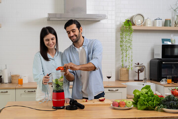 Young couple mixing fruit in a food processor, making a smoothie. Husband and wife having fun with smoothie in the kitchen and looking at each other.