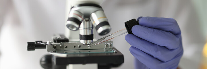 Scientist works with pipette and microscope in research laboratory.