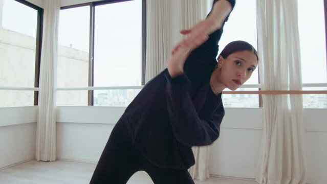 Young artistic girl looking at camera, performing impulsive fast movements and graceful turns during expressive contemporary dance in studio