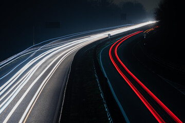 Abstract image of night traffic lights on the road. Car light trails at night in curve asphalt road. Long exposure showing movement of cars from bridge or drone - obrazy, fototapety, plakaty