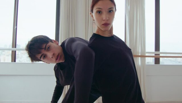 Young stylish couple in black clothes looking at camera and performing expressive contemporary dance in a studio. Zoom shot