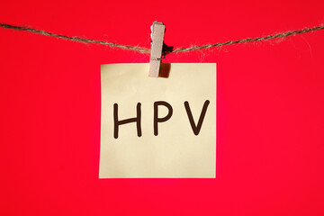 HPV Human papillomavirus text on a yellow sticker hanging on a rope with clothespins on a red background