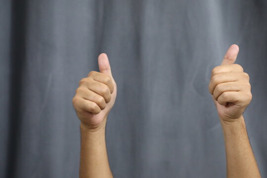 Two male hands showing thumbs up on a gray background with copy space