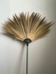 A natural grass broom leaned against the wall.