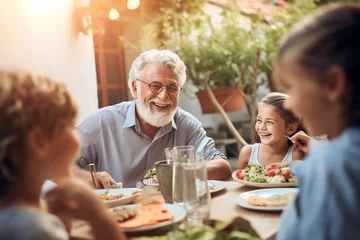 Fotobehang Happy Senior Grandfather Talking, eating and Having Fun with His Grandchildren, Holding Them in Lap during Outdoor © Salsabila Ariadina