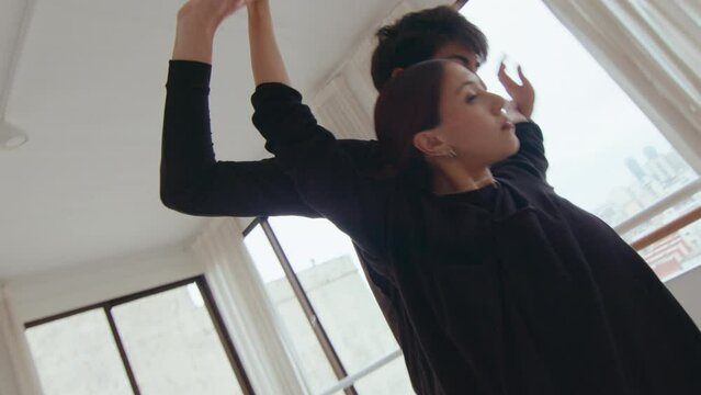 Young beautiful duet performing sensual contemporary dance, practicing partner tricks on a rehearsal at studio. Handheld camera shot