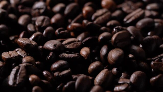 Close-up video of roasted coffee beans. Moving sideways. Dropping coffee beans.