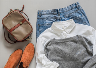 Comfortable women's clothing - mom's jeans, white cotton shirt, gray pullover, suede boots, cross body bag on a gray background, top view