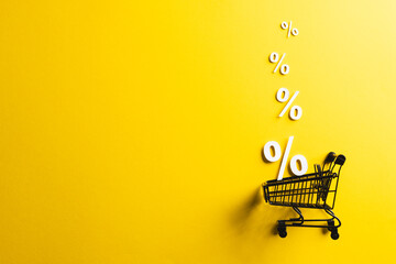 Shopping trolley and white percent signs with copy space on yellow background
