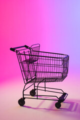 Vertical image of shopping trolley with copy space over neon purple background