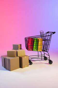 Vertical image of shopping trolley with bags, boxes and copy space over neon purple background