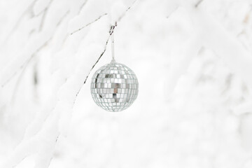 A disco ball hanging on a snowy tree branch