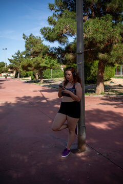 young beautiful woman leaning on a lamppost looking at her smartphone