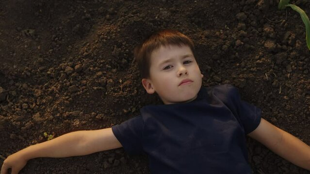Top view of a Cheerful boy with brown hair, and a black t-shirt lying on down on the ground in the garden. Healthy lifestyle - children in the nature and