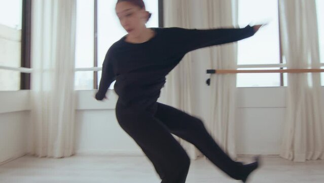Young artistic girl performing energetic movements during contemporary dance rehearsal at the studio. Zoom shot, handheld camera