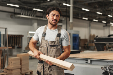 Young carpenter man looking and choosing wood plank at workshop in carpenter wood factory