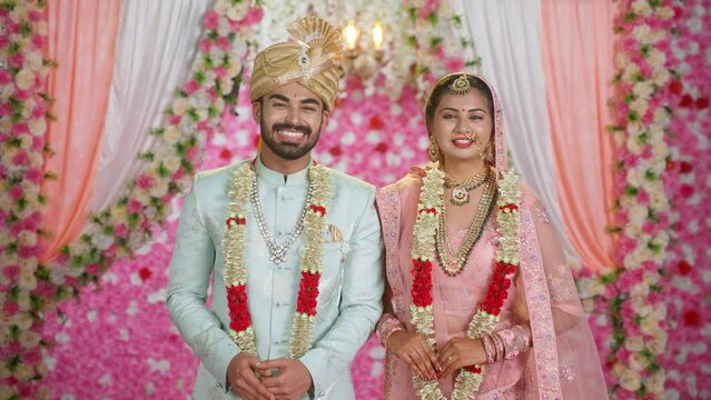 Happy similing Indian Bride and groom posing to camera on wedding stage in traditional ethnic wear - concept of Cultural Celebration, joyful marriage and Ceremony.