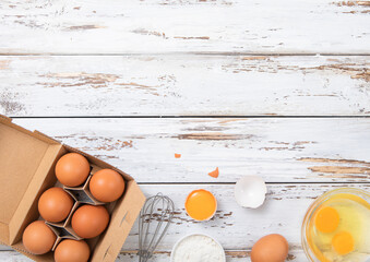 Brown raw farmers eggs with yolk,whisk and shell on light wooden table background.