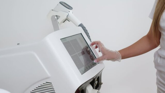 A dermatologist stands with equipment for laser hair removal. Cosmetologist adjusts device settings for laser hair removal procedure