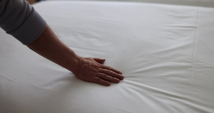 Visitor hand touching white sheets of double bed in hotel suite. Tourist enjoying touching fine white sheets in hotel bedroom slow motion
