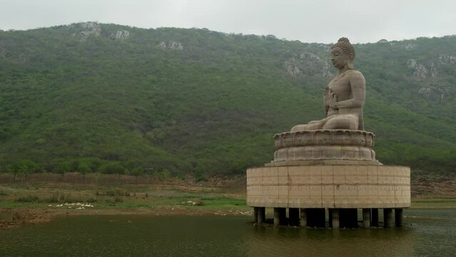 70 foot high Buddha statue at Ghora Katora lake surrounded by mountains under hazy sky, Rajgir, Bihar, India