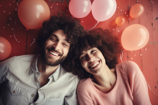 Picture of man and woman laying on ground with colorful balloons in background. This image can be used to depict romantic or playful moment between two people.