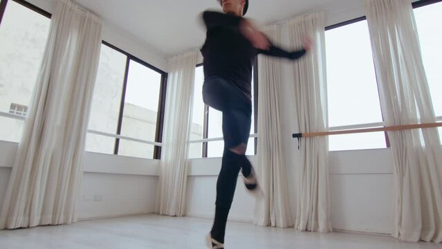 Young professional male dancer practicing ballet pirouettes alone in the studio. Zoom shot, low angle view