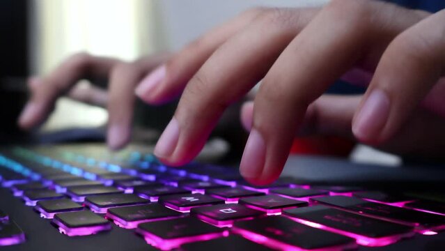Closeup view of male hands typing on a gaming laptop keyboard with RGB backlit. Journalist writing article, programming, coding, modern business, freelancing, browsing, gaming, writing email.