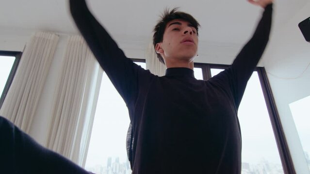 Young Latin male dancer doing passe, developpe and arabesque while performing ballet movements during rehearsal in studio. Zoom shot