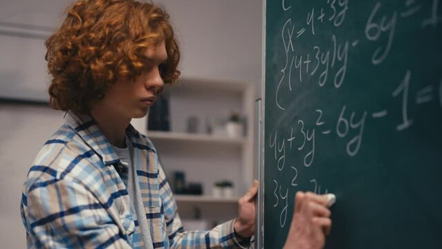 Confident teenage boy solving algebra equation on chalkboard, good at math