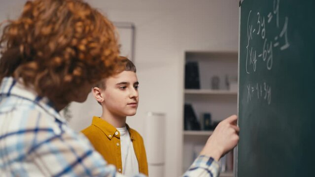 Schoolboy helping classmate with a math problem, solving equation on board