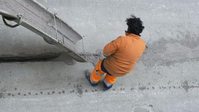 Worker Shoveling Fresh Cement pre-mixed concrete in the track, which drips from the hopper of a mixer truck