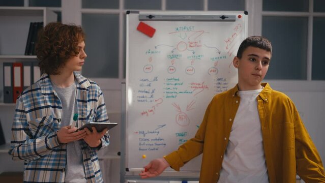 Two teen boys presenting their project in front of classmates, technology class