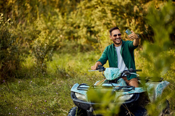 A man having an adventure driving a quad bike and taking a selfie with his phone. © bnenin