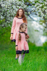 Fototapeta premium mother and daughter walk through a blooming apple orchard