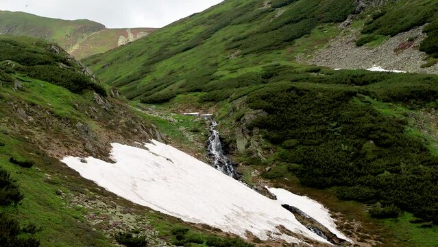 Waterfall in Rodnei National Park, Maramures, Romania, Europe. Lala Mare lake waterfall in springtime with snow on the mountains