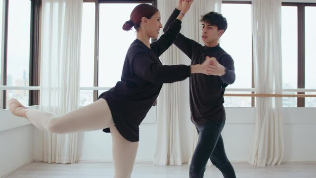 Pair of young ballet dancers holding hands, performing pirouettes and talking during rehearsal in the studio. Zoom shot