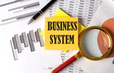 BUSINESS SYSTEM text on a sticky on the graph background with pen and magnifier