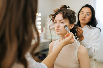 Close-up of unrecognizable female makeup artist applying highlighter on cheekbones for face...