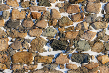 Old stone wall covered with snow. Weathered rough masonry surface. Texture for background and design.