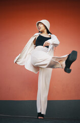 Woman kick, fashion and city wall with freedom, hipster style and urban clothes with confidence. Red background, traveling and stylish female person in town with cool and modern outfit and thinking