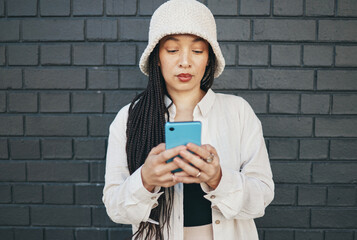 Girl with phone, brick wall and urban fashion, typing social media post, chat or internet search. Streetwear, gen z girl or online influencer with smartphone for content creation and communication.
