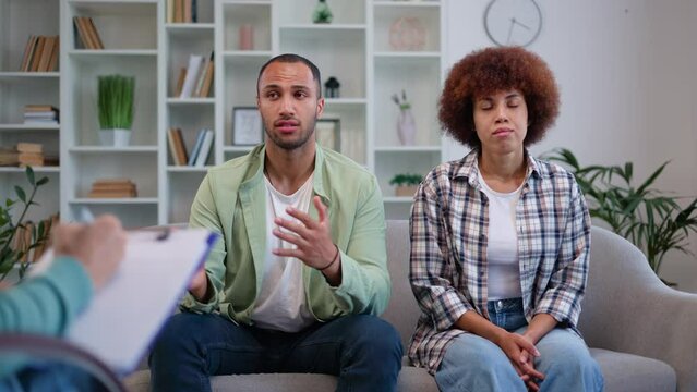 African american husband and wife facing family issues and asking psychologist for help in modern clinic. Casually dressed woman feeling devastated while man talking and complaining on bad attitude.