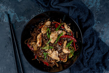 Asian wok noodles with chicken and vegetables with chopsticks on the table. - 648060969
